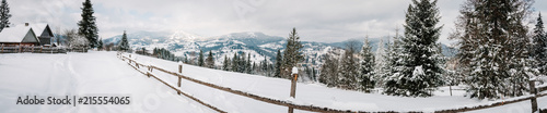Snow-capped wooden fence, houses in mountains Carpathians Ukraine. On background Christmas tree in forest. Winter nature. Landscape. Top side view. Long edge. Panorama. Bukovel.