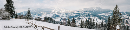 Snow-capped wooden fence in mountains Carpathians Ukraine. On background Christmas tree in forest. Winter nature. Landscape. Top side view. Long edge. Panorama. On background of forest and ski slopes.