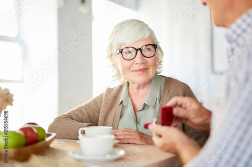 Senior woman looking at her husband showing ring in small velvet box for anniversary