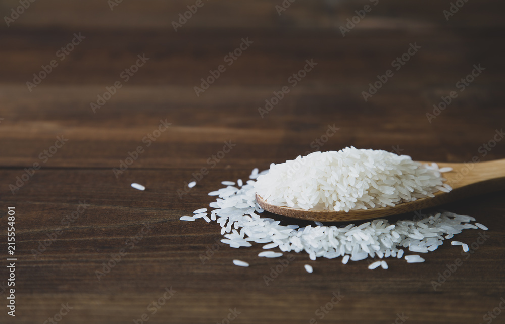 White jasmine rice with wooden spoon on wooden background White jasmine rice with wooden spoon on wooden background