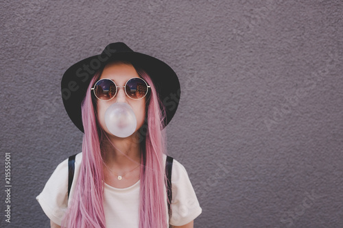 Young hipster woman with long pink hair blowing a bubble with bubble gum. photo