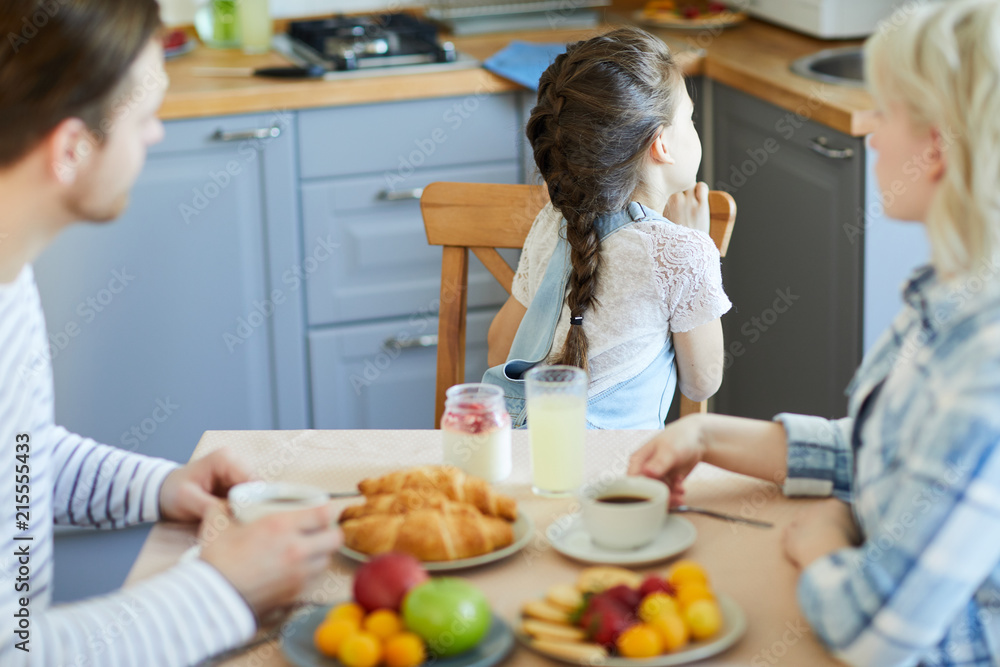Little offended or capricious girl turned from her parents by breakfast