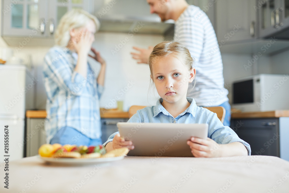 Obraz premium Unhappy little girl with touchpad looking at camera while her parents having argument