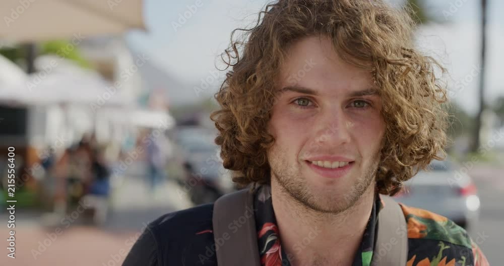 close up portrait of happy young man smiling enjoying warm summer vacation in busy urban beachfront wearing backpack close up portrait of happy young man smiling enjoying warm summer vacation in busy urban beachfront wearing backpack