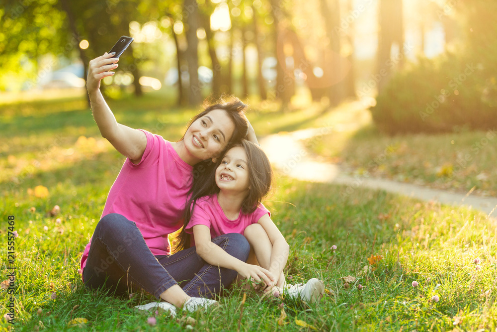 Young mother with pretty daughter make photo in park Young mother with pretty daughter make photo in park