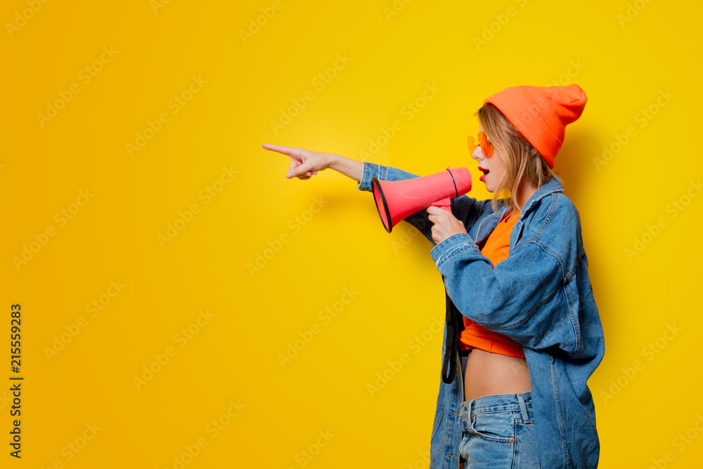 Young style girl in jeans clothes with pink megaphone on yellow background. Symbolizes female resistance. Clothes in 1980s style Young style girl in jeans clothes with pink megaphone on yellow background. Symbolizes female resistance. Clothes in 1980s style