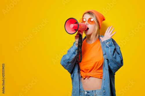 Young style girl in jeans clothes with pink megaphone on yellow background. Symbolizes female resistance. Clothes in 1980s style photo