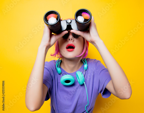 Young style girl in purple clothes with binoculars on yellow background. Clothes in 1980s style