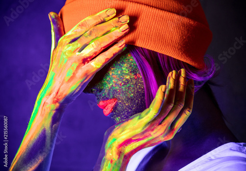 Young girl in hat with fluorescent paint on lips and face. Studio shot.
