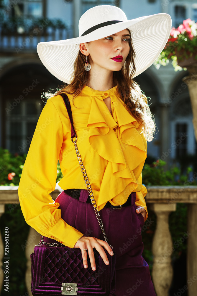 hypothese noot Terugroepen Outdoor fashion portrait of young beautiful woman wearing stylish white  hat, yellow blouse with frills, violet trousers, holding velvet quilted  bag, posing in street, near old european architecture Stock Photo | Adobe