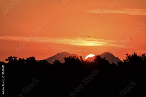 Sun setting behind mountains and birds crossing the scene  red sky.