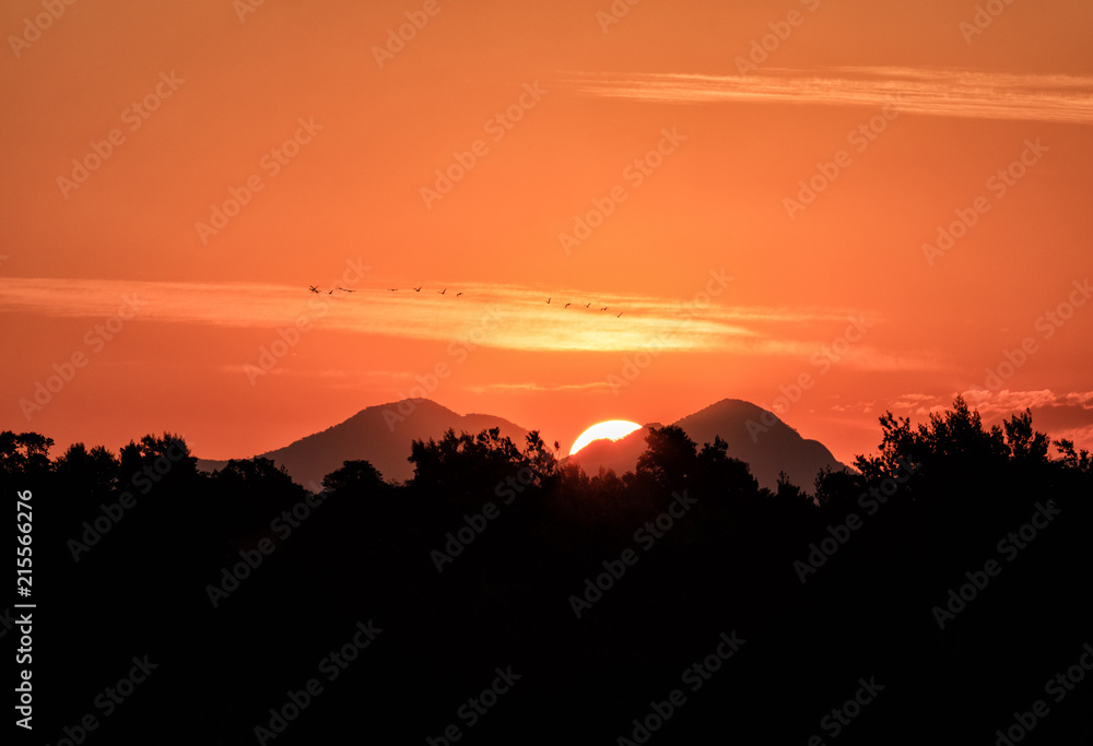 Sun setting behind mountains and birds crossing the scene, red sky. Sun setting behind mountains and birds crossing the scene, red sky.