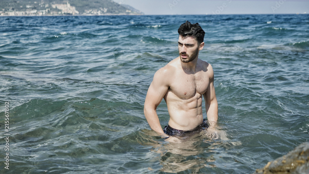 Handsome muscular young man standing on a beach, relaxed, shirtless Handsome muscular young man standing on a beach, relaxed, shirtless