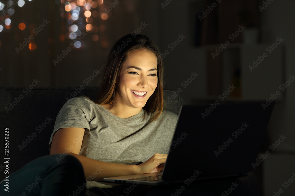 Happy lady using a laptop in the night Happy lady using a laptop in the night