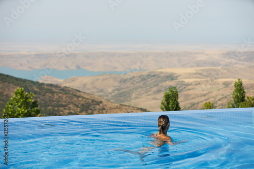 Young woman relaxing in infinity swimming pool looking at nature landscape on background, outdoor © Gecko Studio