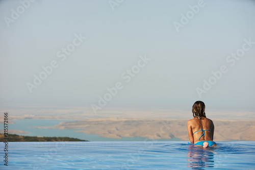 Young woman relaxaing in the swimming pool looking at the nature landscape view on background. Travel  summer holiday concept