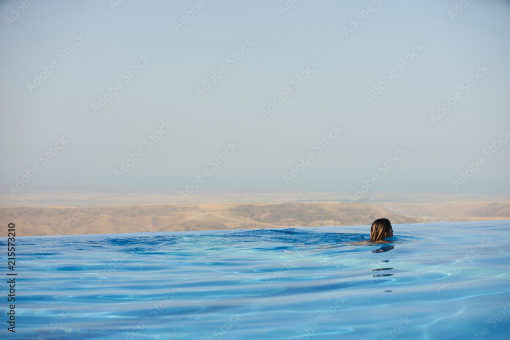Relaxing woman in luxury hotel pool on holidays vacation travel. Young female person enjoying in infinity pool spa at hotel resort in an exotic paradise getaway.