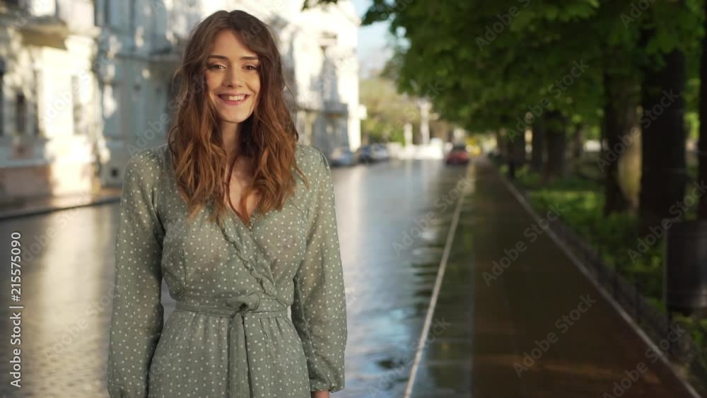 Portrait of cheerful beautiful woman 20s wearing summer dress smiling, while walking through empty boulevard on sunny day slow motion Portrait of cheerful beautiful woman 20s wearing summer dress smiling, while walking through empty boulevard on sunny day slow motion