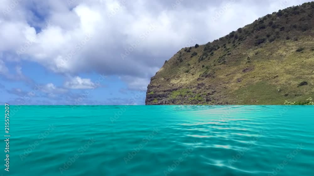 A glimmering tropical ocean with light flickering off the surface faces a tropical island in Hawaii during daytime. A glimmering tropical ocean with light flickering off the surface faces a tropical island in Hawaii during daytime.