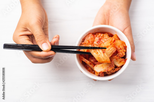 Hand holding kimchi cabbage in a bowl and chopsticks for eating, top view, Korean food