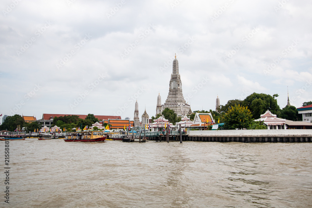 Obraz premium Wat Arun buddhist temple . famous ancient grand palace in Bangkok Thailand , asian travel landmark . old historic architecture . Chao phraya river with boats . beautiful clear sky and clouds
