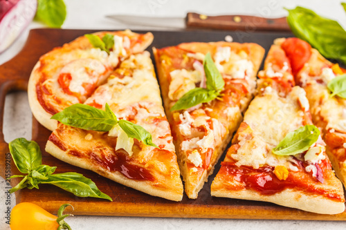 Oval homemade pizza with feta cheese, tomatoes and basil on a wooden board.