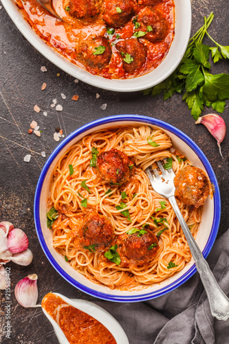 Pasta with meatballs in tomato sauce with parsley and garlic in white dish, top view, dark background.
