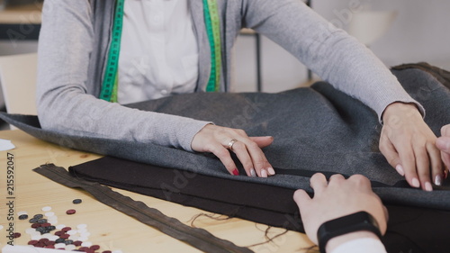 Close-up of a hands of tailored fashion designers working with materials, they sitting at the beautiful atelier with different tailoring tools and clothes. Two tailors createn a new collection of
