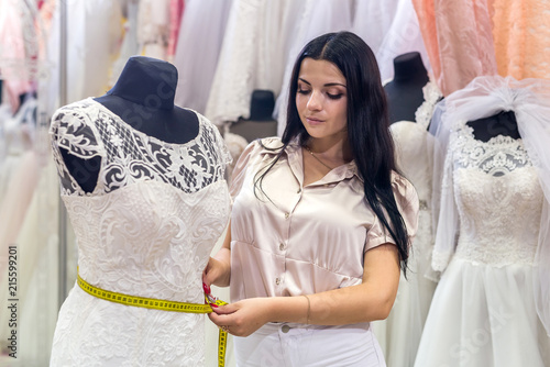 Brunette woman seller measuring details of wedding dress