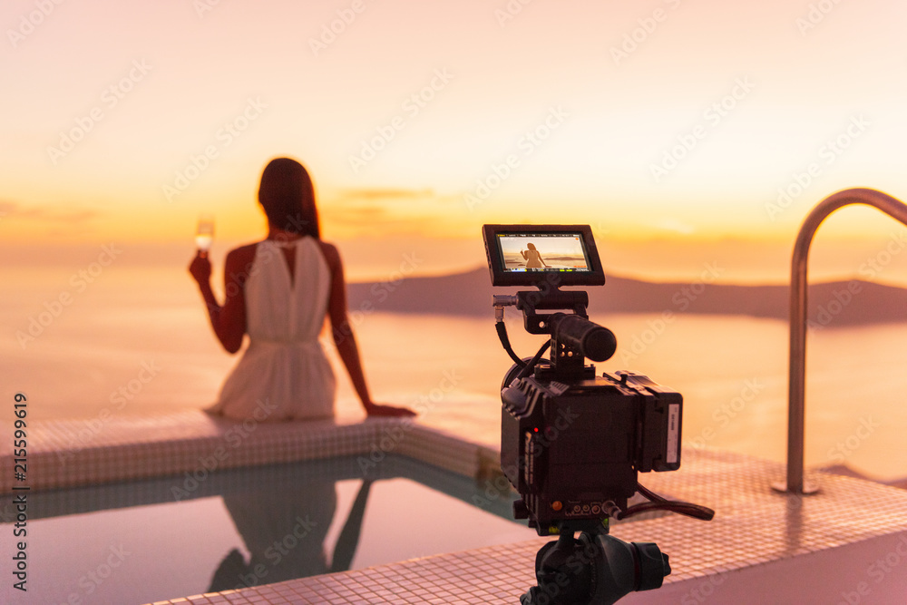 Obraz premium Video camera filming actress woman acting for movie on luxury hotel location behind the scenes of shoot. Professional videography equipment shooting outdoor at sunset.