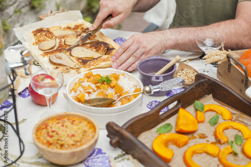 rice with pumpkin and honey on the table and other autumn food, pie with pear. Delicious family dinner in the courtyard. Men's hands cut the cake. Copy space