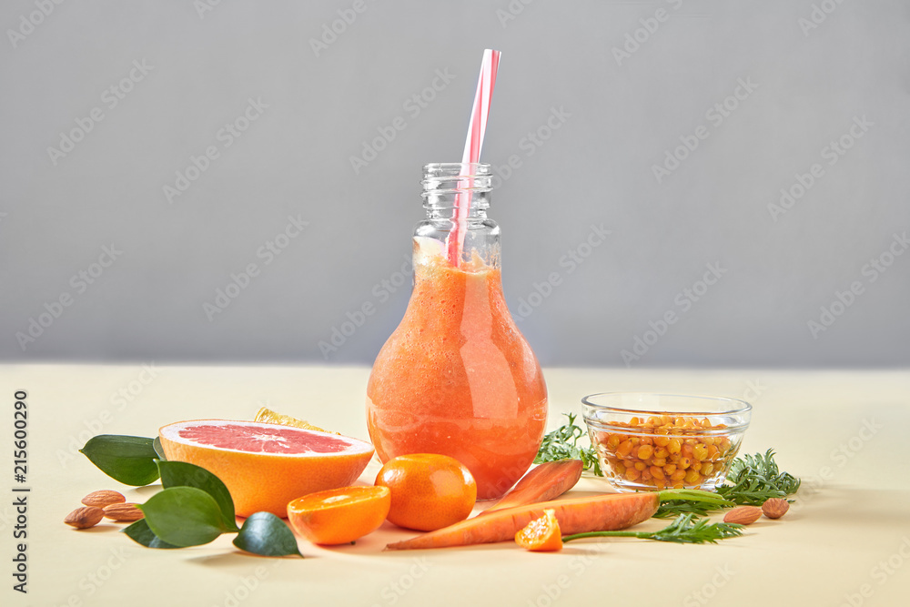 Φωτογραφία Homemade orange smoothies with carrot, grapefruits, sea buckthorn, almonds in glass bottle on a yellow paper background