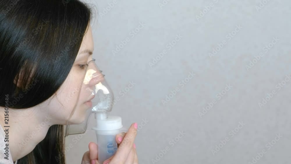 Use nebulizer and inhaler for the treatment. Closeup woman's face inhaling through inhaler mask. Side view. Use nebulizer and inhaler for the treatment. Closeup woman's face inhaling through inhaler mask. Side view.