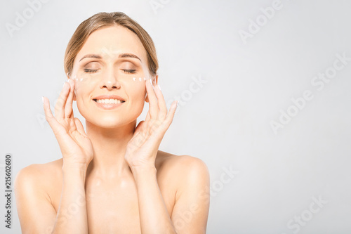 Portrait of young beautiful woman smiling while taking some facial cream isolated on white background with copy space.