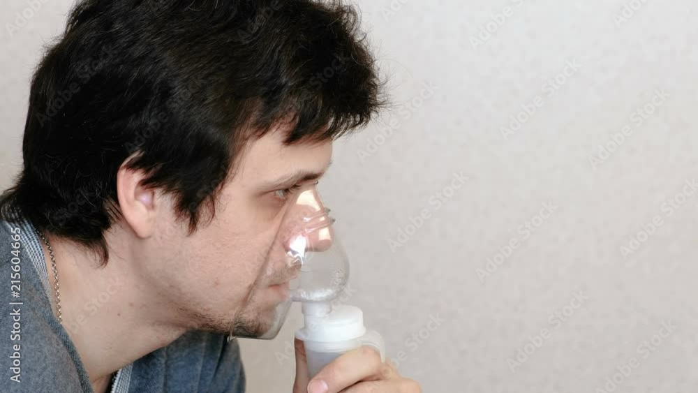 Use nebulizer and inhaler for the treatment. Young man inhaling through inhaler mask. Side view. Use nebulizer and inhaler for the treatment. Young man inhaling through inhaler mask. Side view.