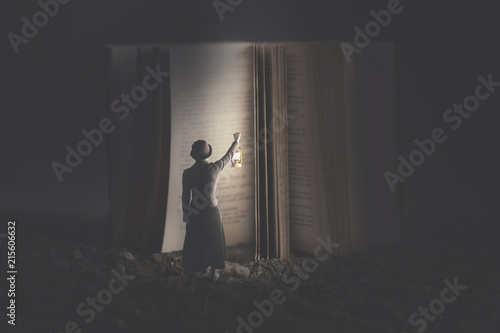 Curious woman illuminates with a lantern a giant book at night