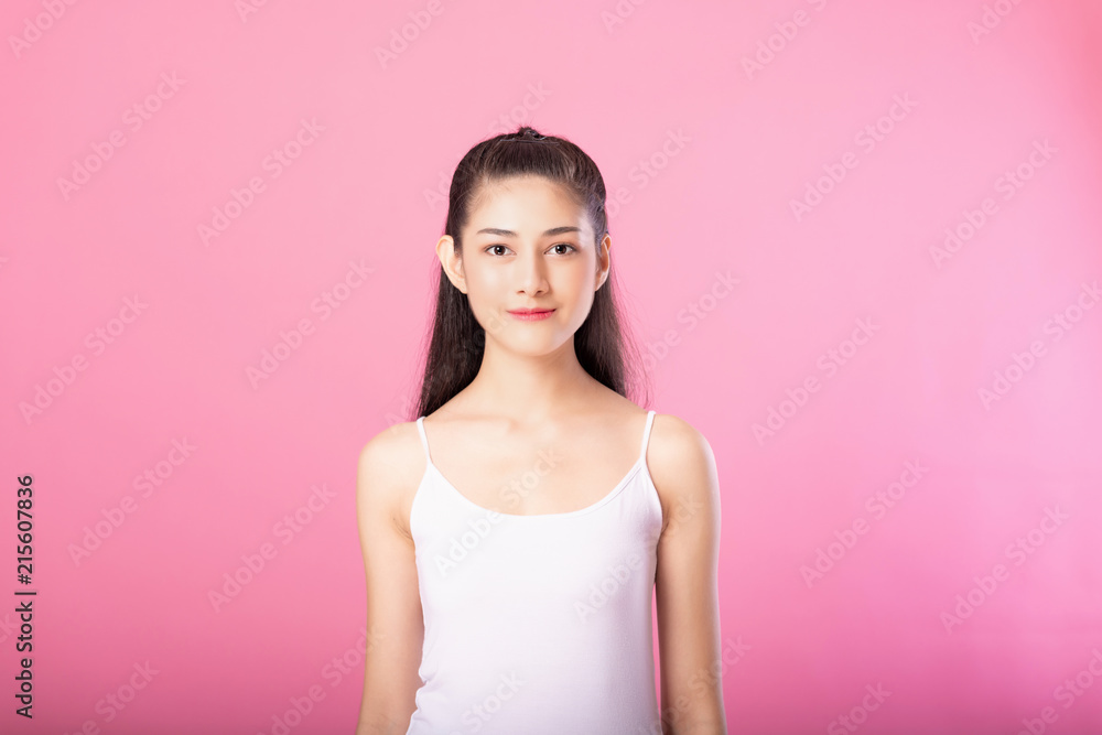 Portrait of a smiling attractive woman in white tanktop outfit posing while standing and smiling at camera isolated over pink background. Portrait of a smiling attractive woman in white tanktop outfit posing while standing and smiling at camera isolated over pink background.