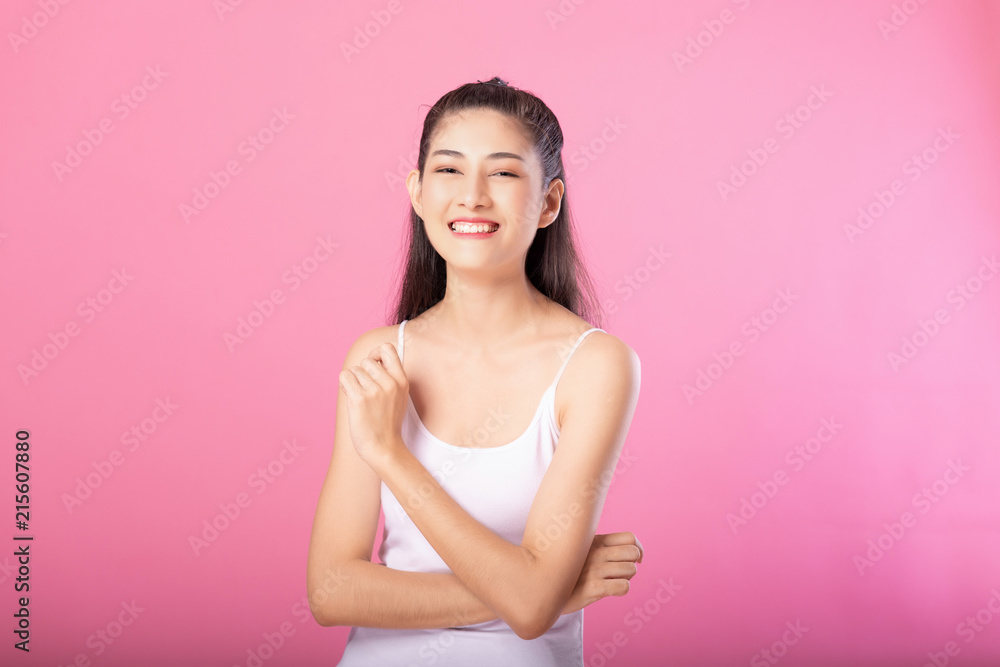 Portrait of a smiling attractive woman in white tanktop outfit posing while standing and smiling at camera isolated over pink background. Portrait of a smiling attractive woman in white tanktop outfit posing while standing and smiling at camera isolated over pink background.