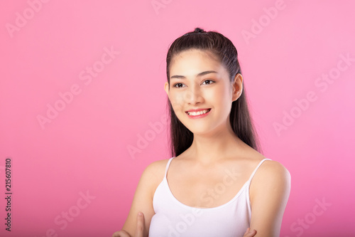 Portrait of a smiling attractive woman in white tanktop outfit posing while standing and smiling at camera isolated over pink background.