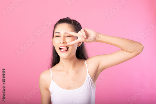 Portrait of a smiling attractive woman in white tanktop outfit with victory pose while standing and smiling at camera isolated over pink background.