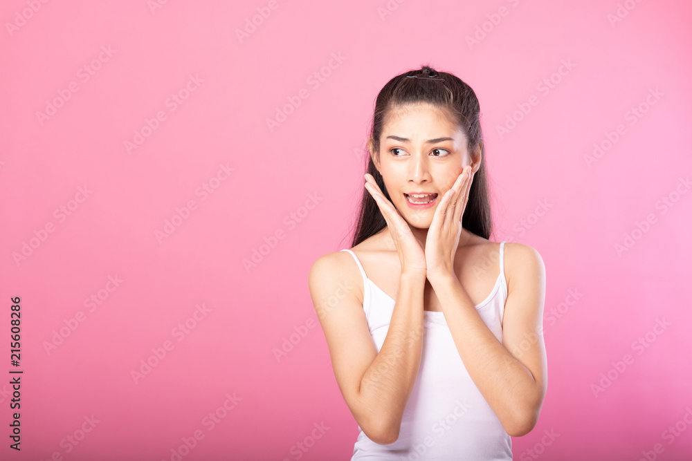 Portrait of a smiling attractive woman in white tanktop outfit with surprise pose while standing and smiling at camera isolated over pink background.
