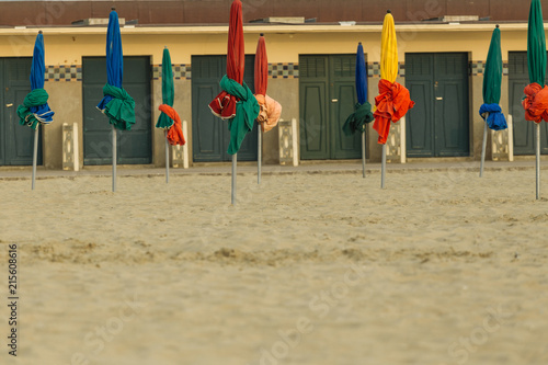 Beach umbrellas on foggy morning in Deauville, fashionable holiday resort in Normandy, France. Beach boxes and folded colorful parasols on the empty beach. Leisure and seaside vacations concept.