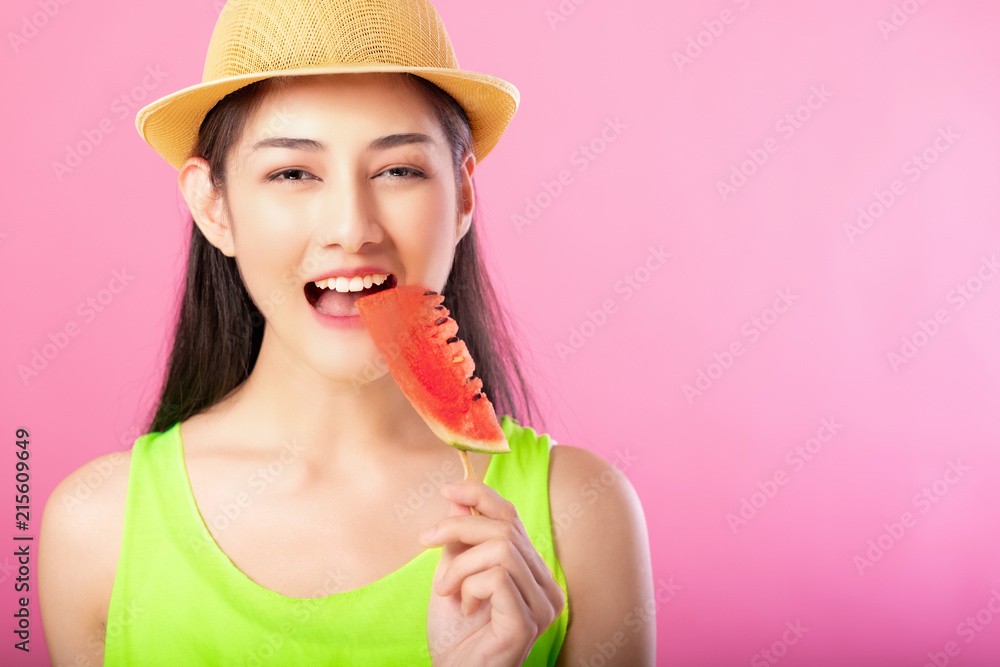Portrait of a happy attractive woman in summer green outfit with hat biting fresh water melon on stick isolated over pink background. Summer vibe concept. Portrait of a happy attractive woman in summer green outfit with hat biting fresh water melon on stick isolated over pink background. Summer vibe concept.