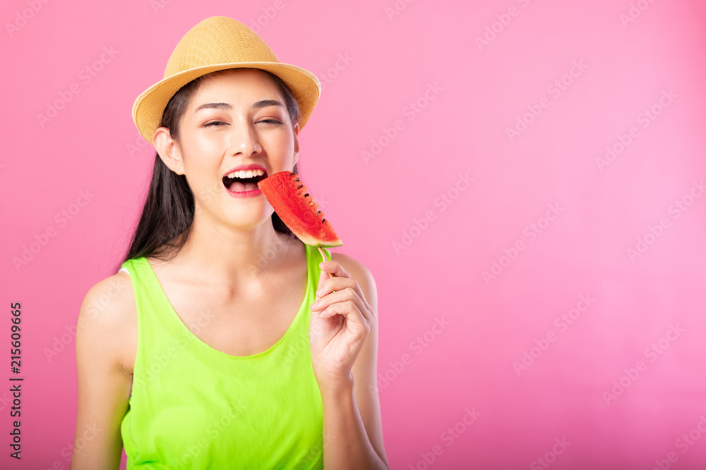 Portrait of a happy attractive woman in summer green outfit with hat biting fresh water melon on stick isolated over pink background. Summer vibe concept. Portrait of a happy attractive woman in summer green outfit with hat biting fresh water melon on stick isolated over pink background. Summer vibe concept.