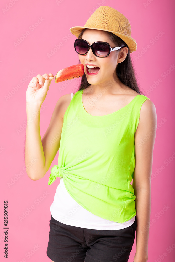 Portrait of a happy attractive woman in summer green outfit with hat and sunglasses biting fresh water melon on stick isolated over pink background. Summer vibe concept. Portrait of a happy attractive woman in summer green outfit with hat and sunglasses biting fresh water melon on stick isolated over pink background. Summer vibe concept.