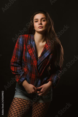 Seductive young woman with long hair posing in checkered jacket on a dark studio background with shadows