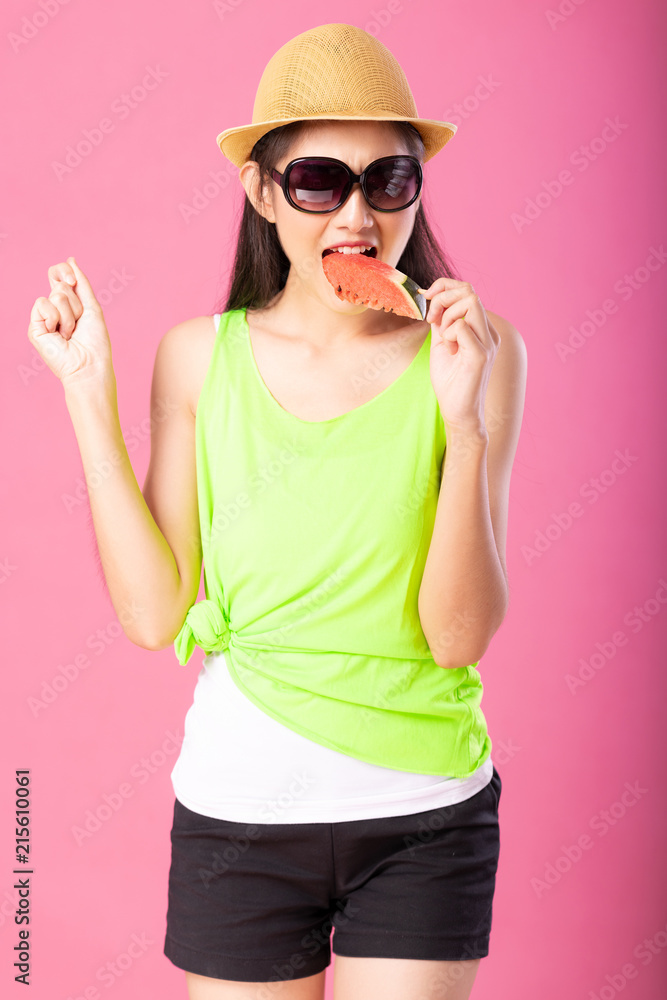 Portrait of a happy attractive woman in summer green outfit with hat and sunglasses biting fresh water melon on stick isolated over pink background. Summer vibe concept. Portrait of a happy attractive woman in summer green outfit with hat and sunglasses biting fresh water melon on stick isolated over pink background. Summer vibe concept.