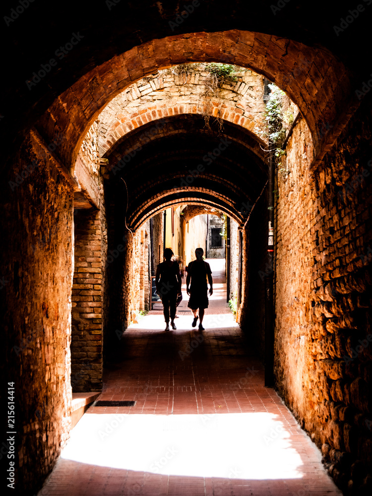 Picturesque medieval narrow street of San Gimignano old town with two person silhouette in the shadow, Tuscany, Italy.