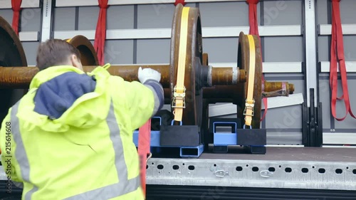 Worker secure the cargo on truck trailer wide view 4K. Dolly slide shot of male person in focus tying up cargo on truck.