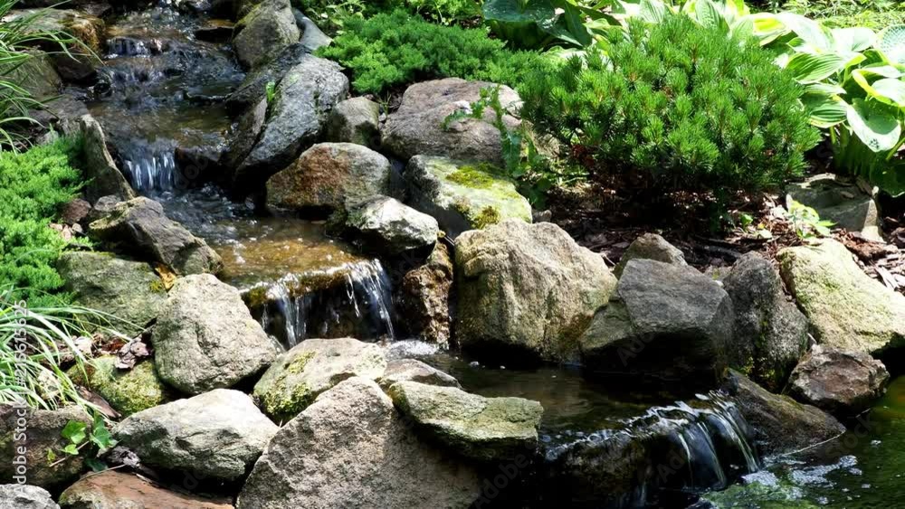 Garden waterfall. Garden pond with water flowers. Beautiful pond in a backyard surrounded with stone during. Garden waterfall. Garden pond with water flowers. Beautiful pond in a backyard surrounded with stone during.